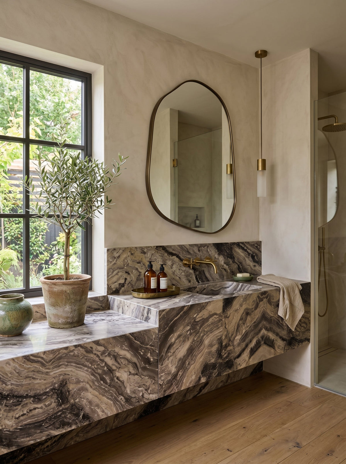 Champagne gold asymmetrical mirror above a marble vanity by a window in a bright bathroom